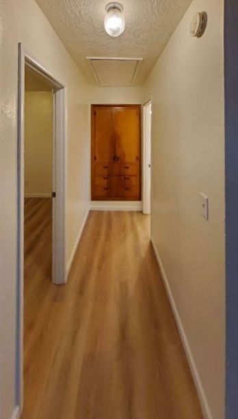 Narrow beige hallway with wood floors and a wooden door at the end