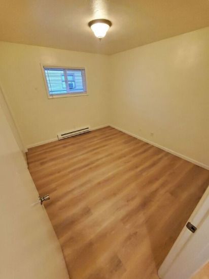 Empty beige bedroom with wood-look flooring, small window, and ceiling light.