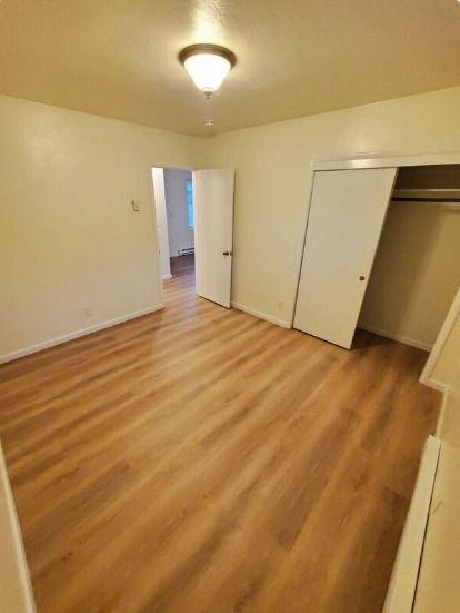 Empty beige bedroom with wood flooring, ceiling light, open doors, and a closet on the right.