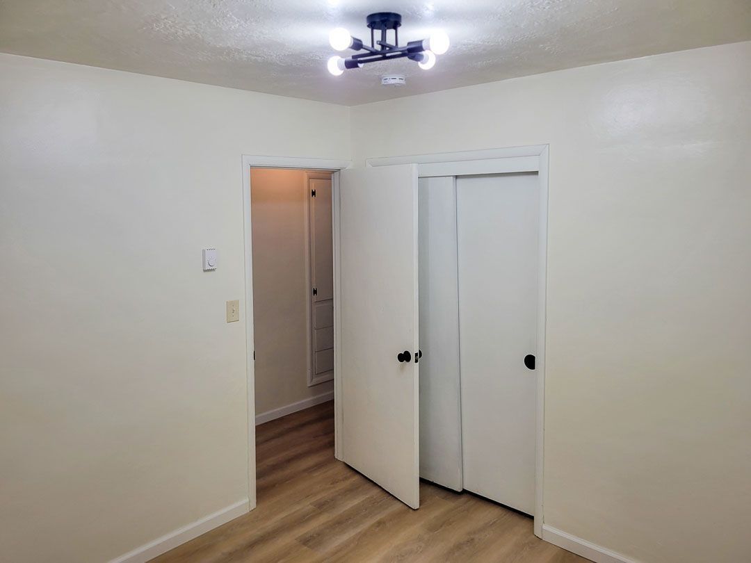 Empty room with beige walls, wood floor, open closet doors, and a lit ceiling fixture
