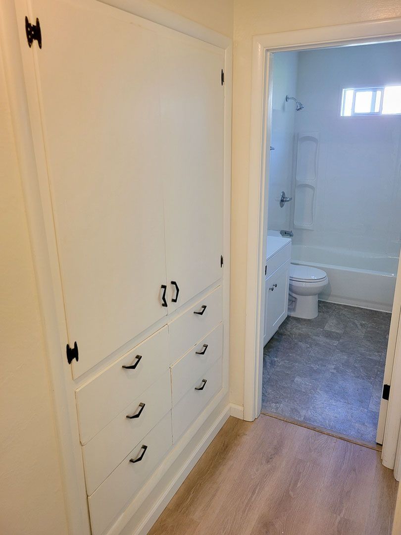 Hallway with white built-in cabinets and open door to a bathroom with a toilet and bathtub.