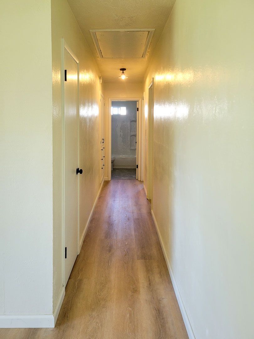 Long narrow hallway with white walls, wood floor, and a light hanging from the ceiling.