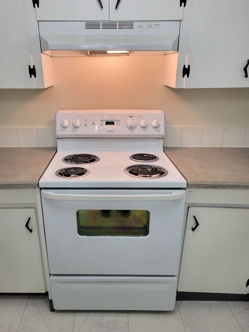 White electric stove centered in a small kitchen with white cabinets and beige countertops.
