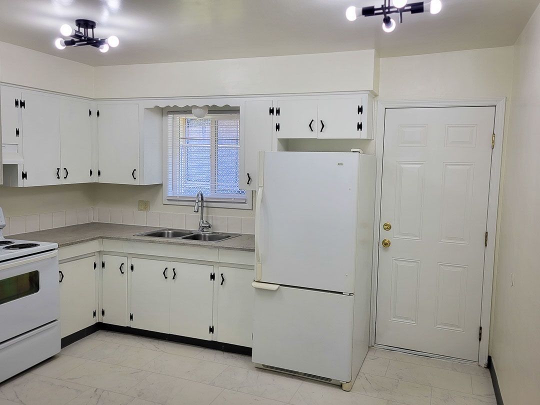 Bright white kitchen with stove, fridge, cabinets, and a window over the sink