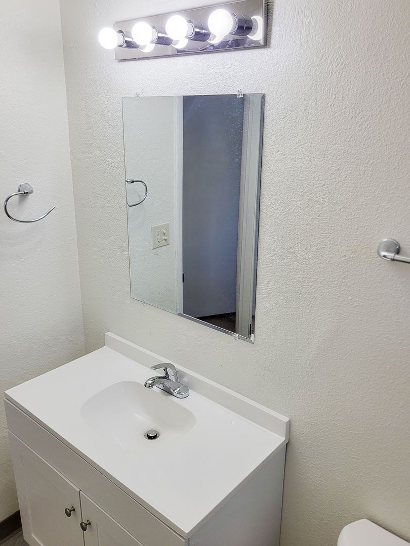 Bathroom vanity with white sink, mirror, and lights above it.