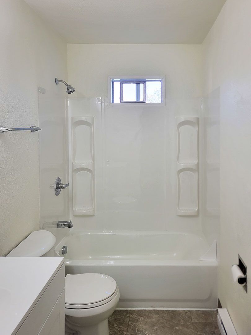 Small white bathroom with a bathtub, toilet, wall-mounted shelves, and a small window.