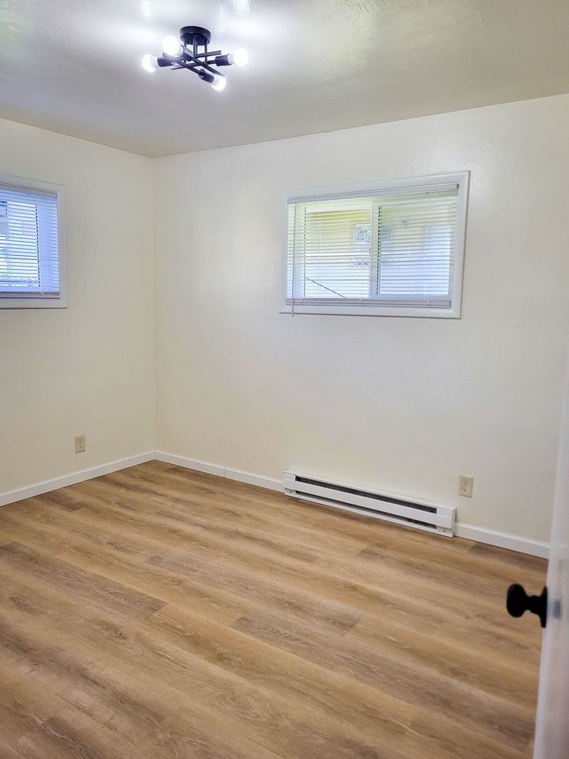 Empty white room with wood flooring, two windows, and a ceiling light.