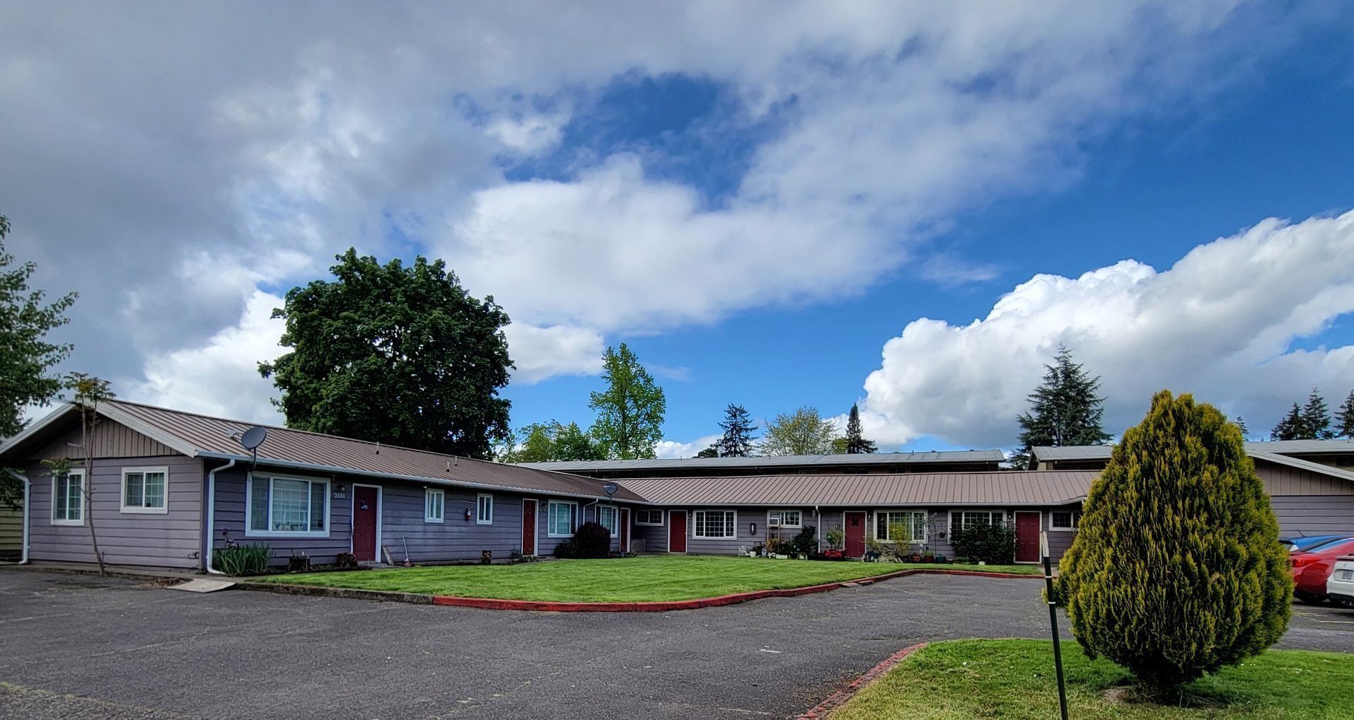 Single-story house with gray siding, red trim, and a gravel driveway under a partly cloudy sky