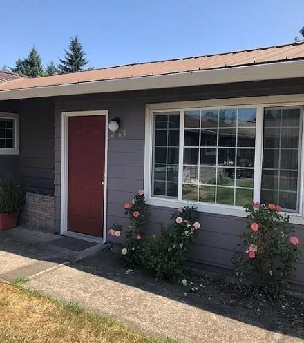 Single-story gray house exterior with red door, large window, and rose bushes along the front walkway