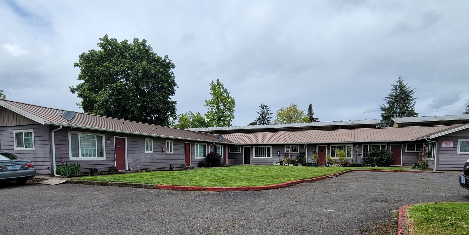 Single-story motel with red doors and gravel parking under a cloudy sky