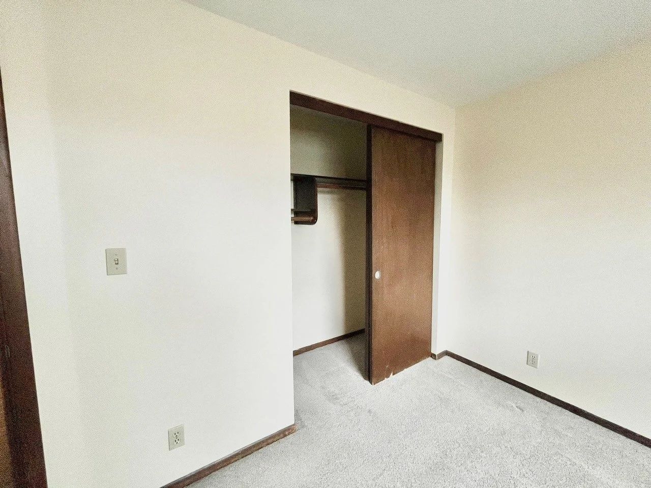 Empty white bedroom with carpet, open closet door, and beige trim