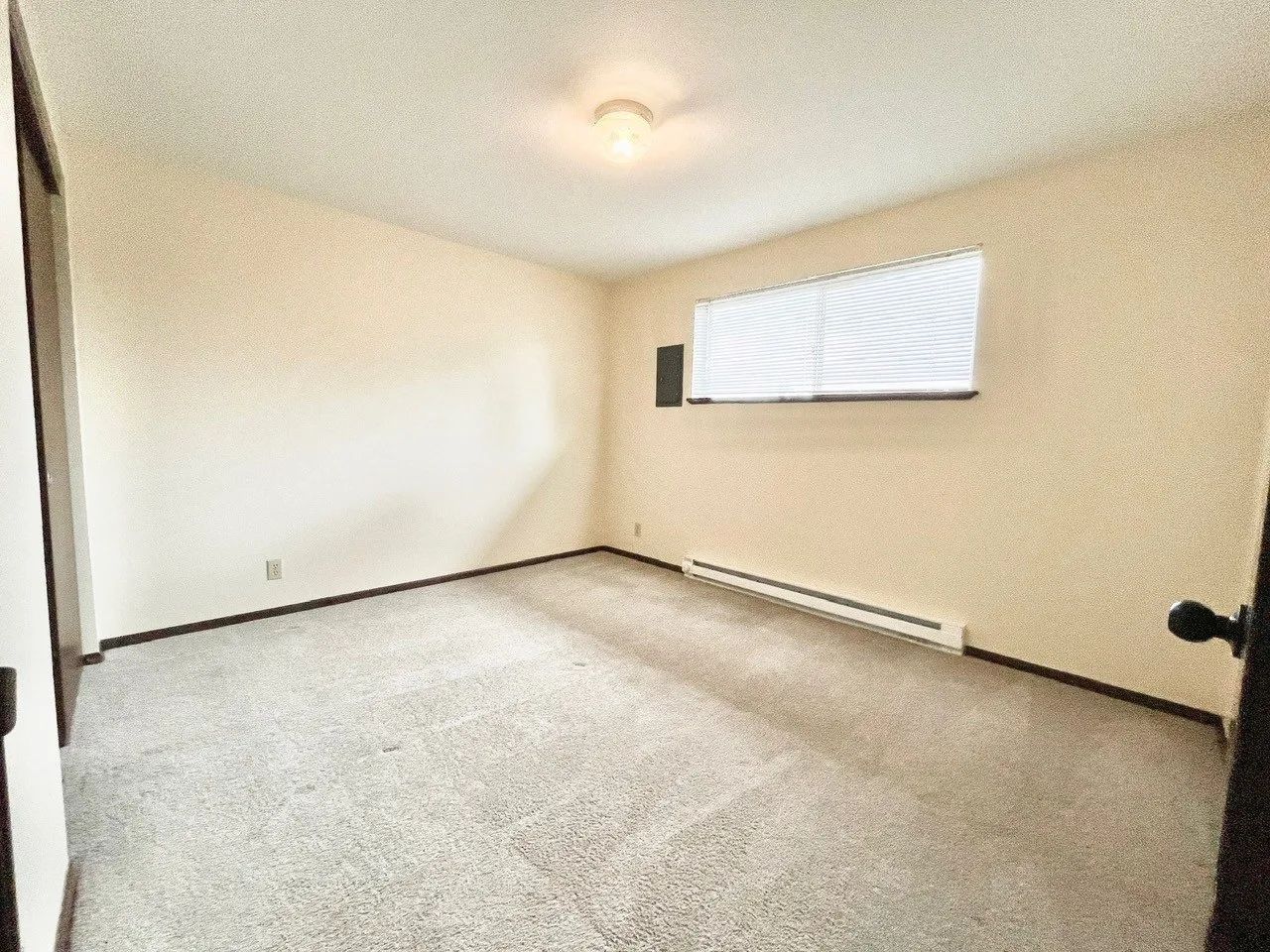 Empty beige bedroom with carpet, small window, and baseboard heater
