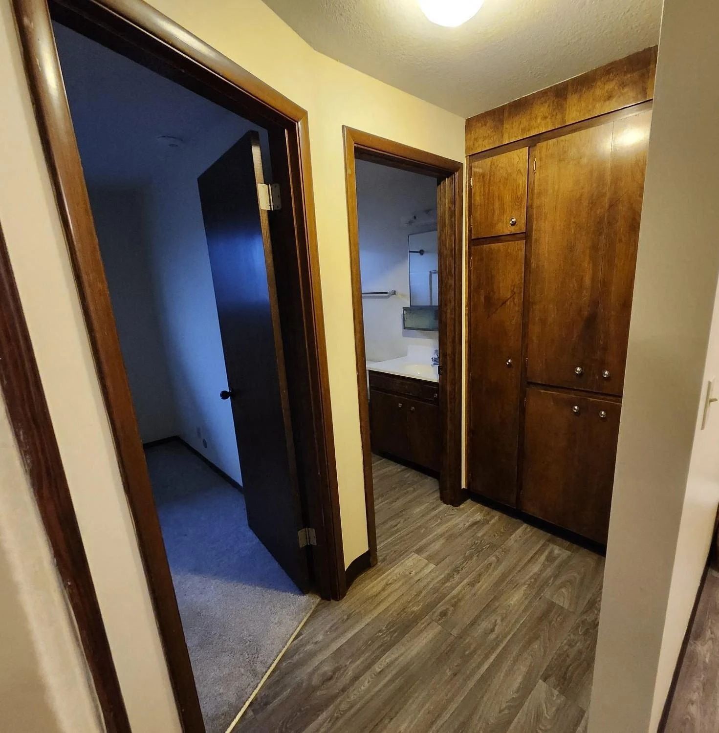 Narrow hallway with wood cabinets, open doors, and a view into adjacent rooms
