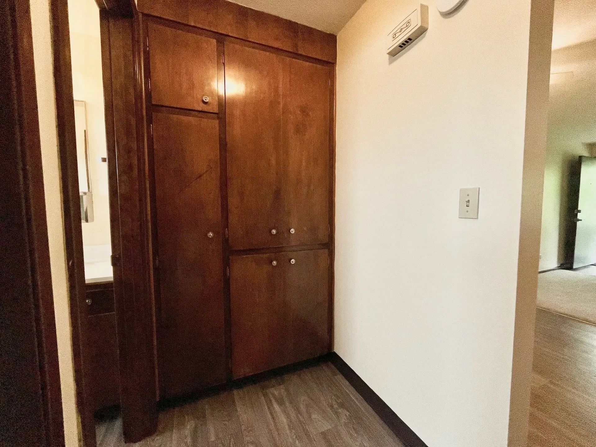 Small hallway with a wooden closet, white walls, and a doorway to a bright room
