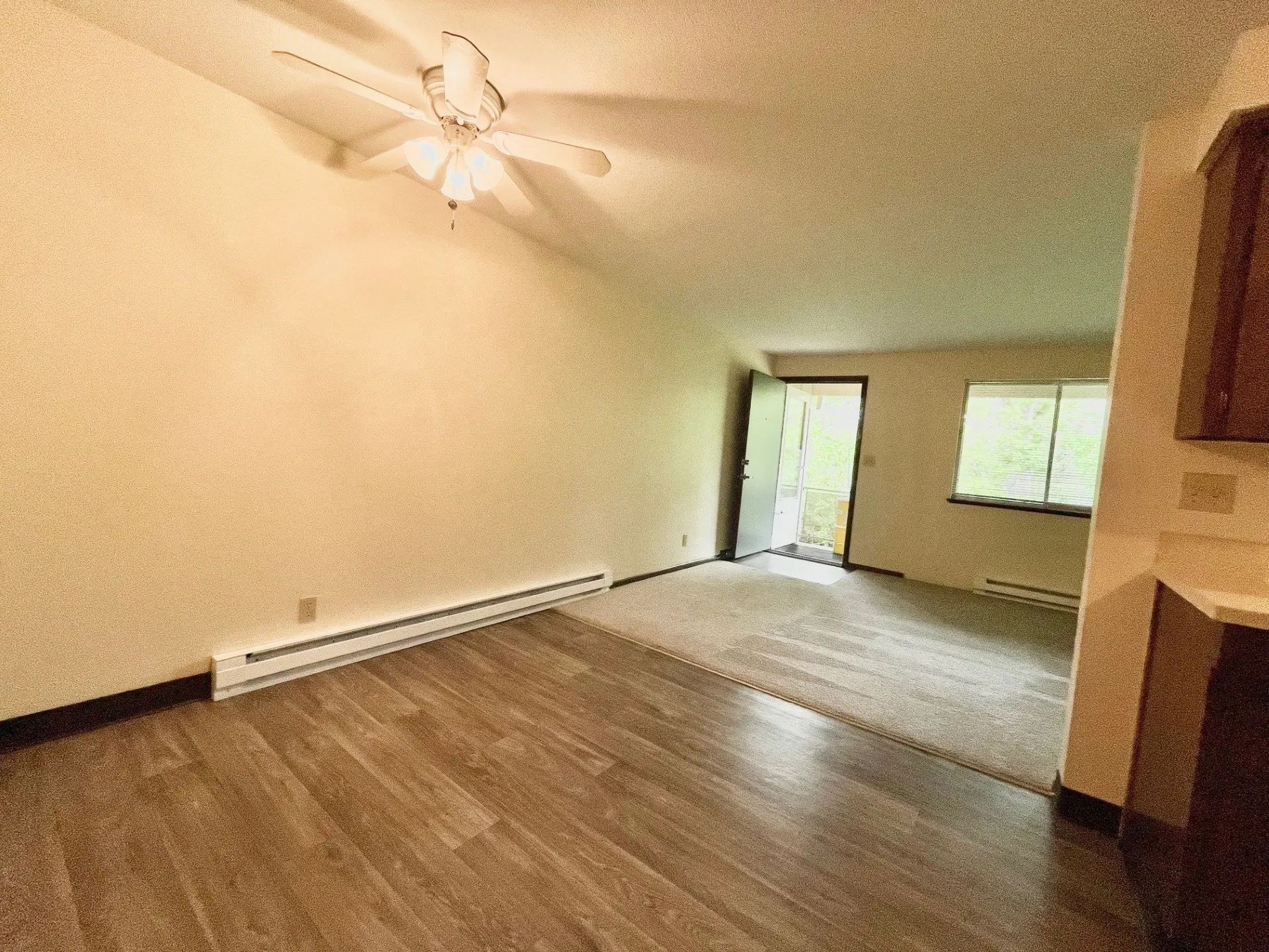 Empty living room with wood floor, ceiling fan, fireplace, and sliding glass door to a bright patio
