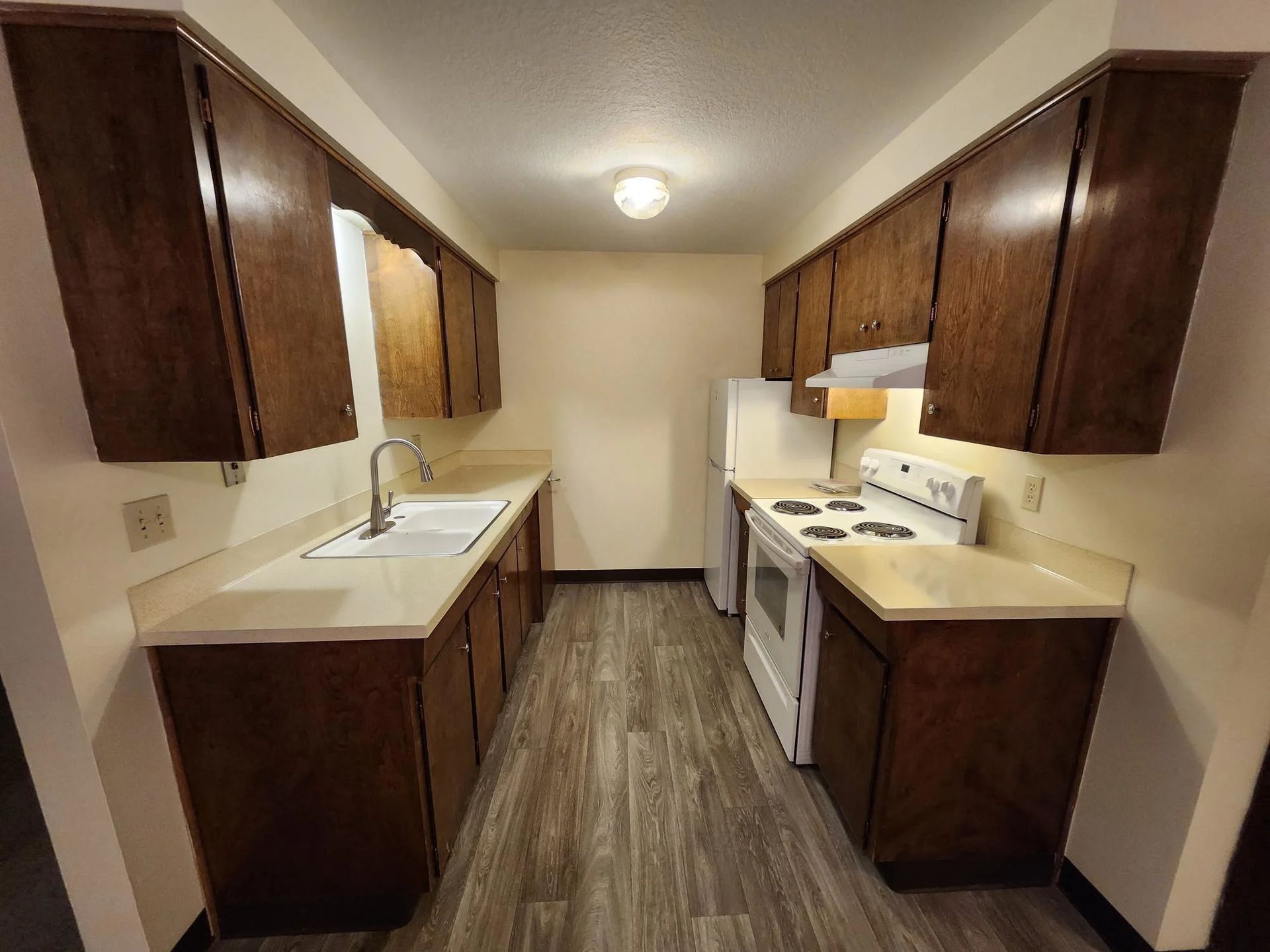 Narrow galley kitchen with dark wood cabinets, white countertops, and wood-look flooring