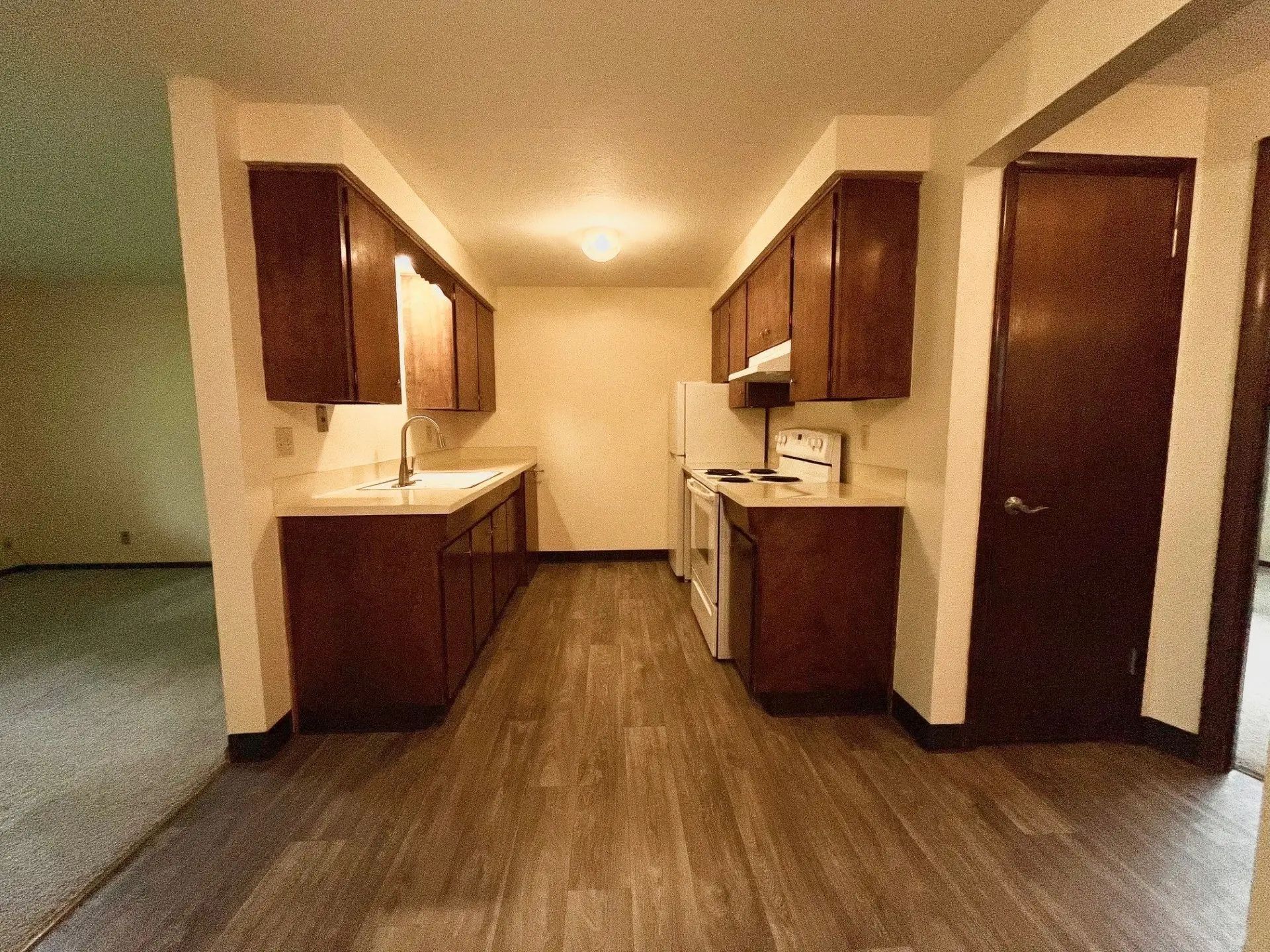 Empty apartment kitchen with dark wood cabinets, white countertops, and wood-look flooring