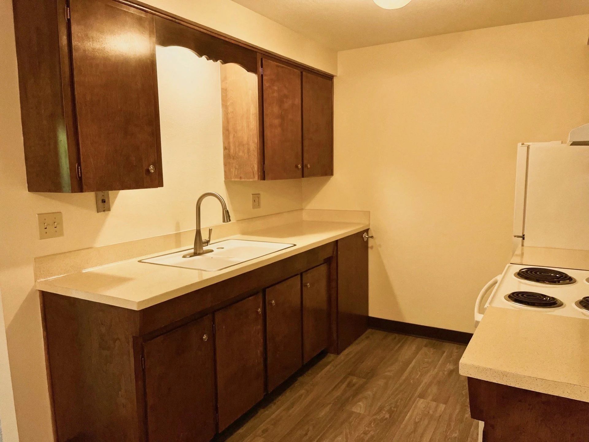 Small kitchen with dark wood cabinets, white countertop, sink, and a stove beside a white refrigerator.