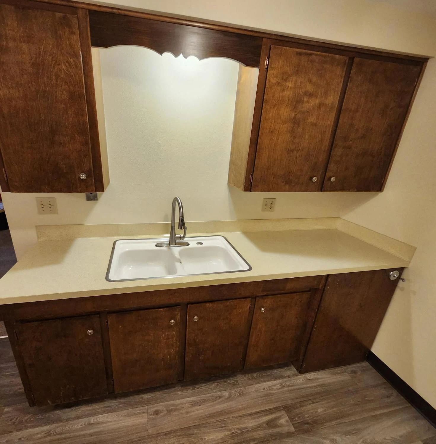 Small kitchen sink area with tan countertops, dark wood cabinets, and a mirrored backsplash.