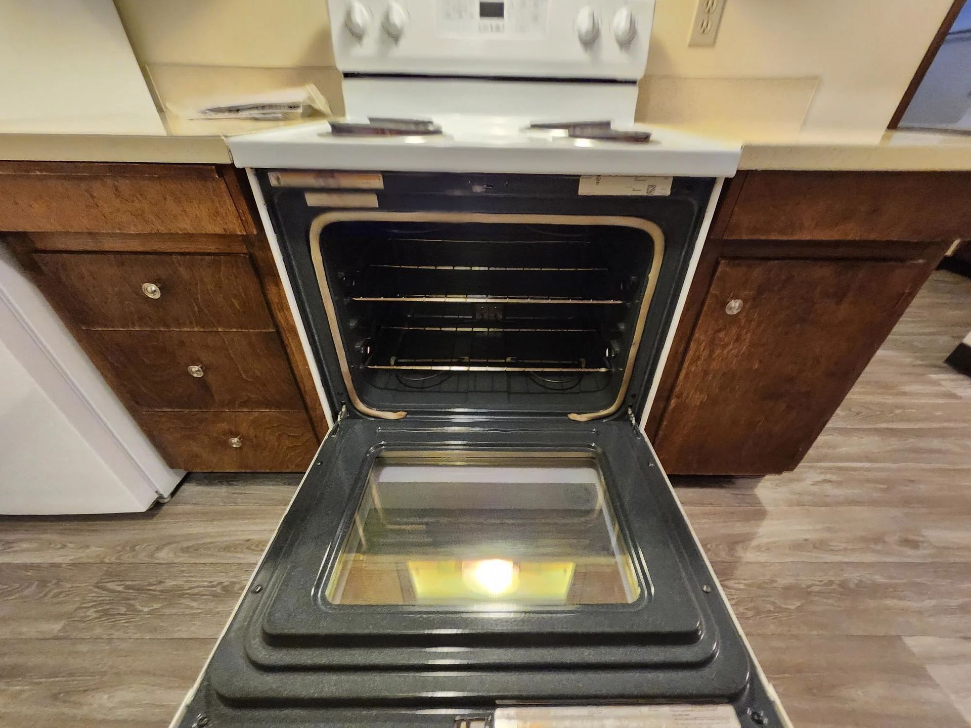 Open oven in a kitchen with a glass door and wooden cabinets on either side.