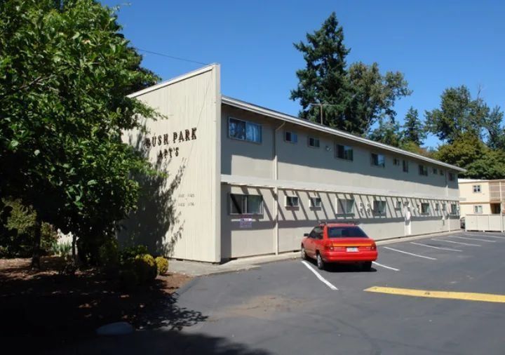 Motel parking lot with a red car beside a beige two-story building and trees