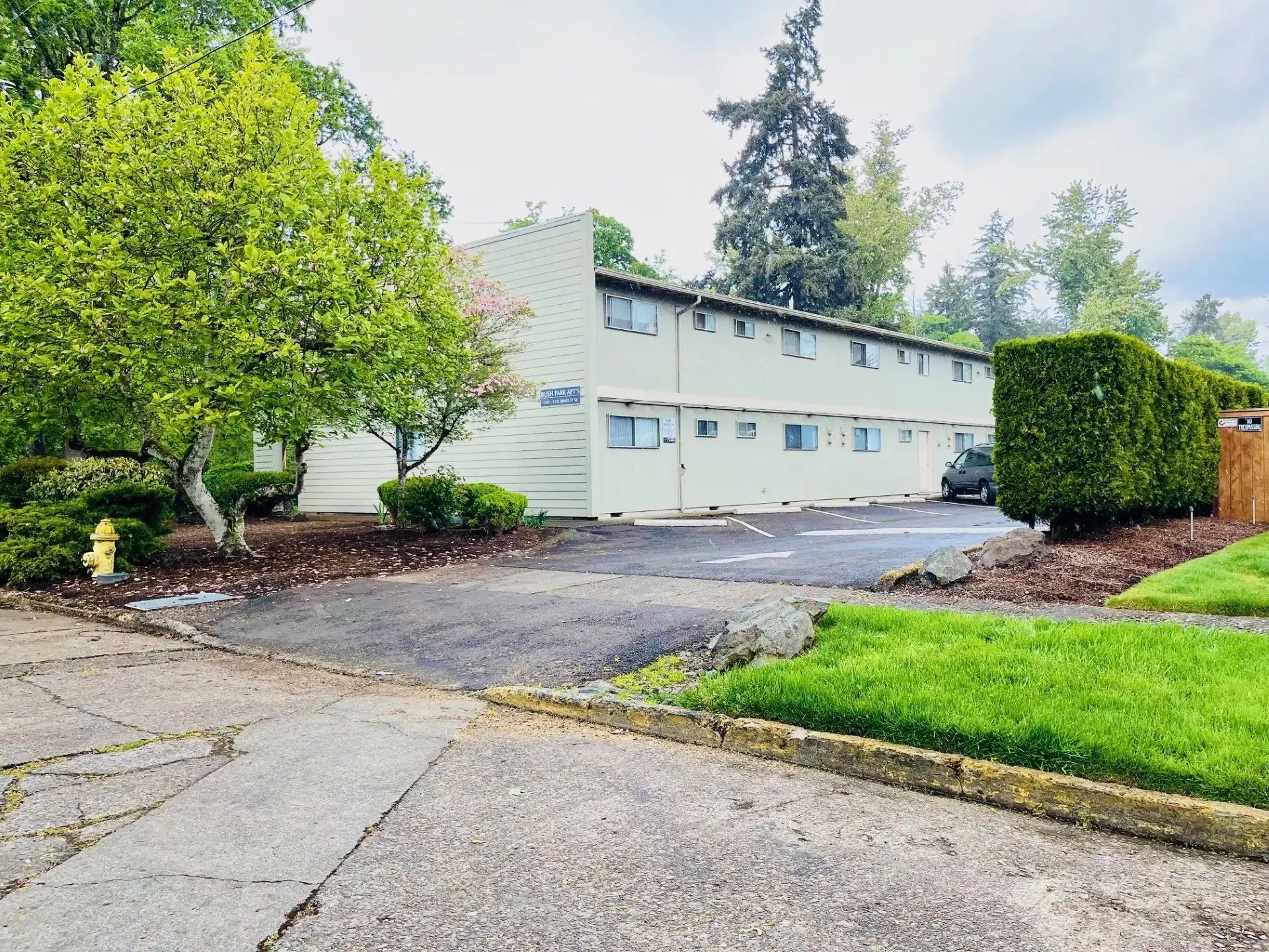 Apartment building beside a driveway and green lawn on an overcast day