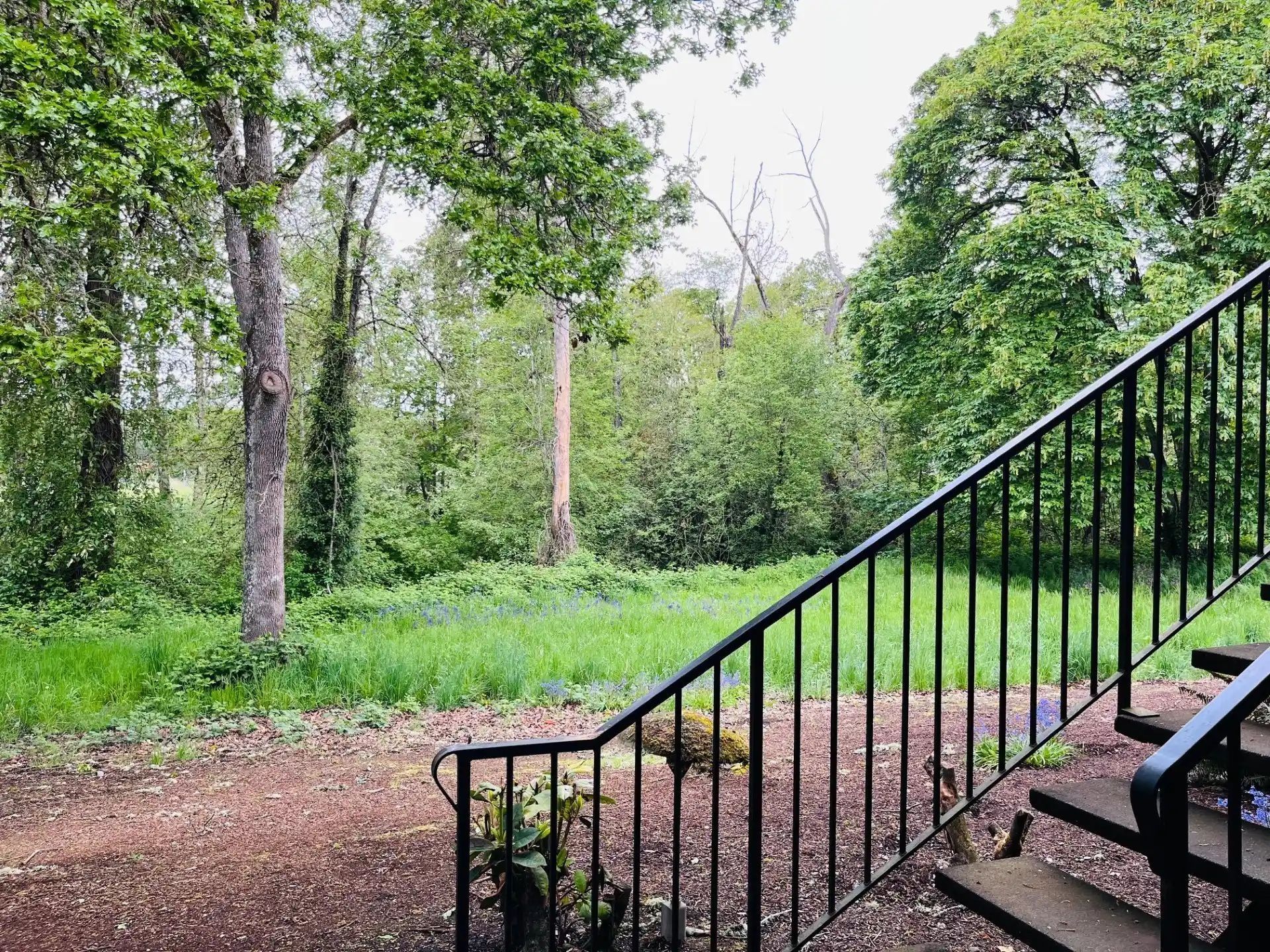 Black metal staircase beside a gravel path, overlooking a green wooded park.