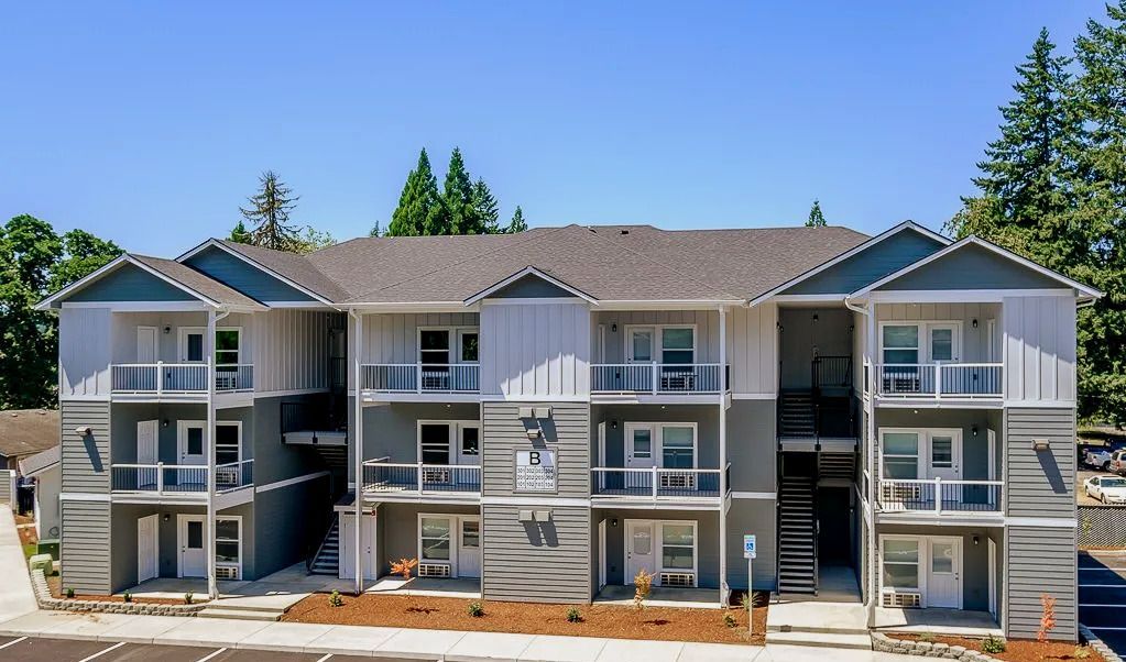 Three-story gray apartment building with balconies and a central staircase under a blue sky