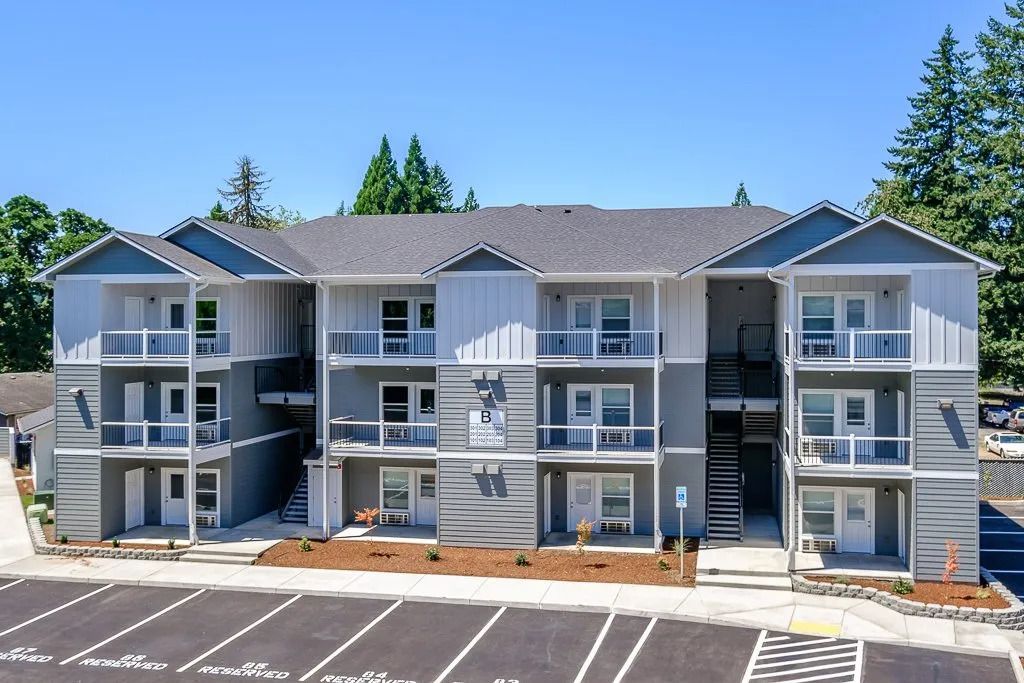 Modern gray apartment building with balconies and parking lot under a clear blue sky