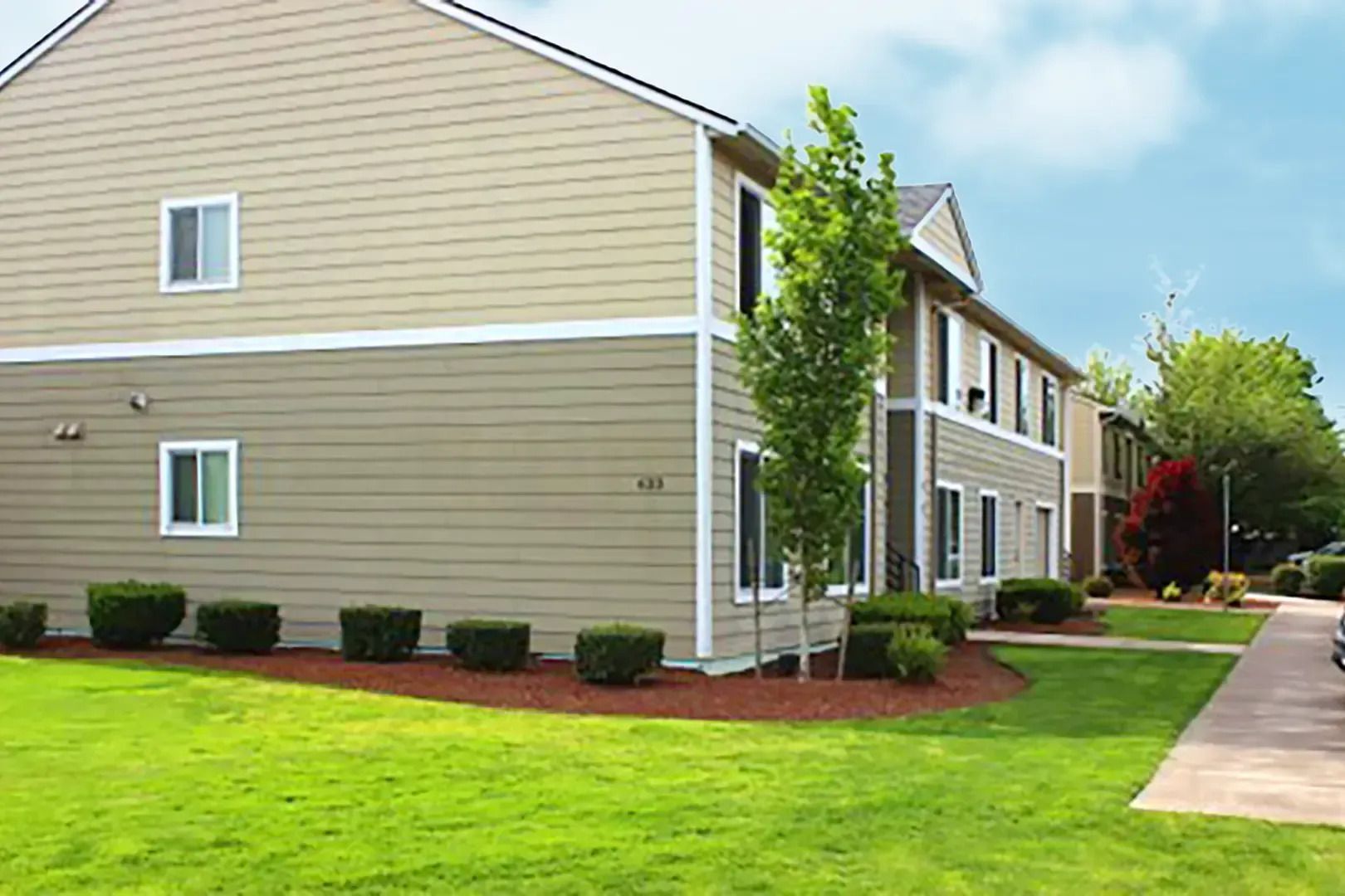 Tan apartment building with white trim, green lawn, and a sidewalk along the side