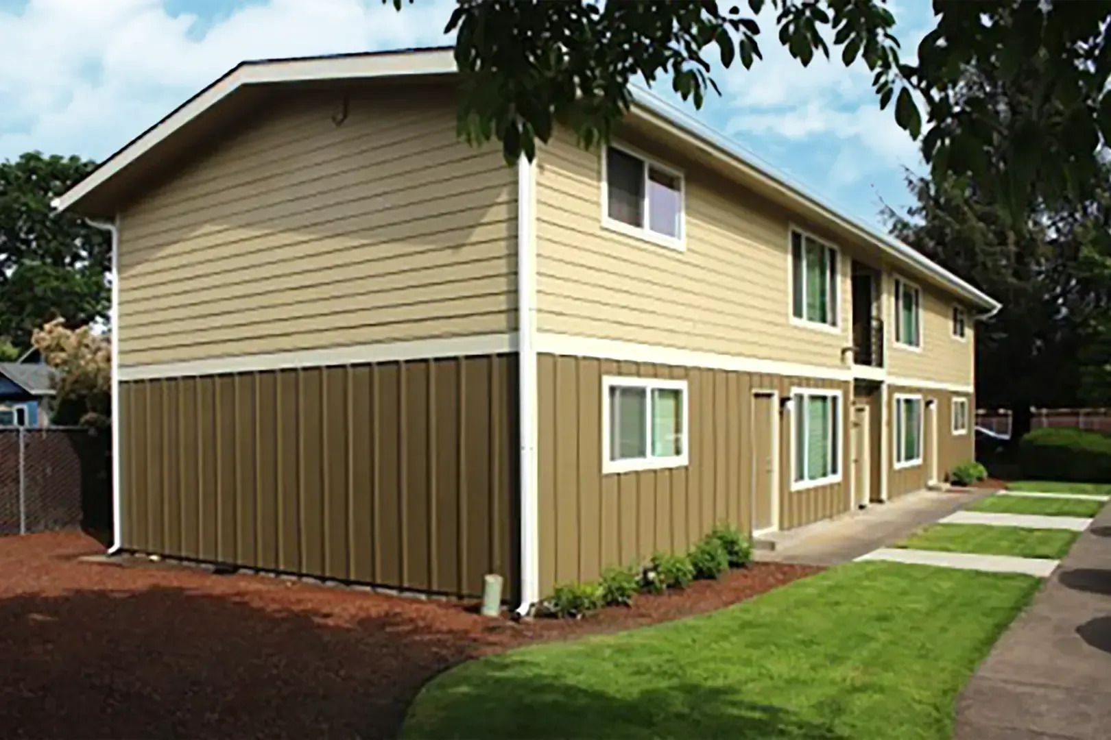 Two-story beige and brown apartment building with white-trimmed windows beside a sidewalk and lawn
