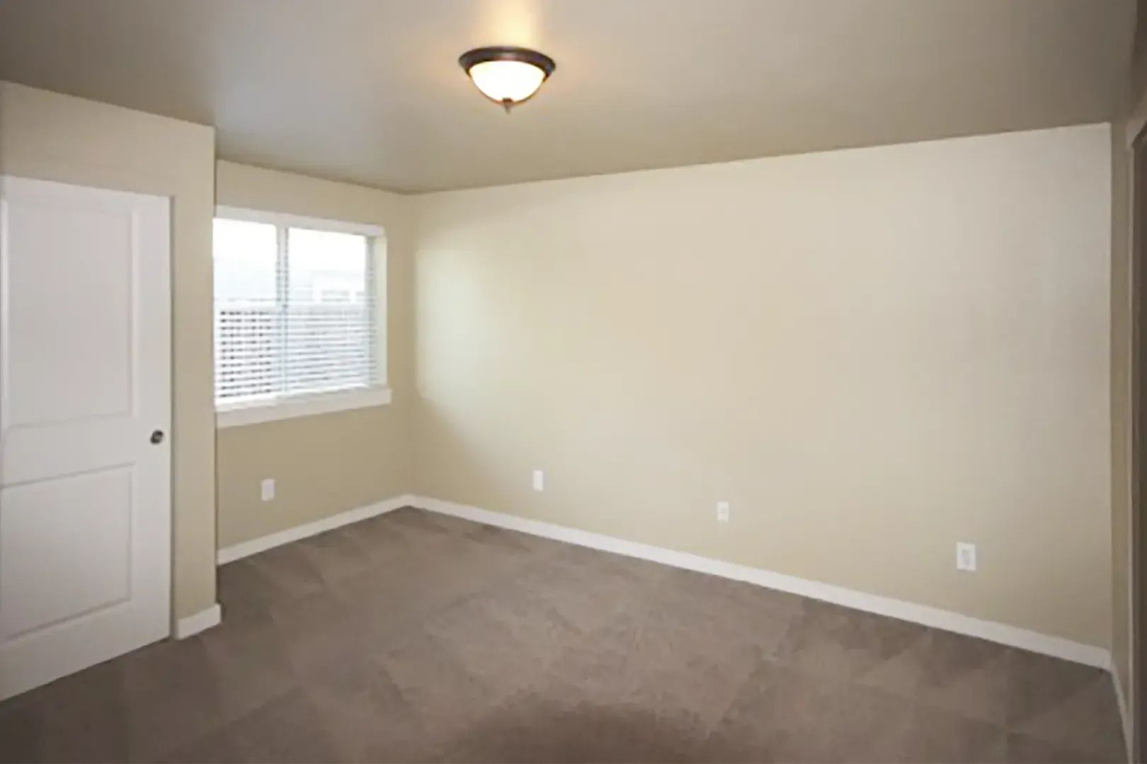 Empty beige bedroom with carpet, a window, closet door, and ceiling light