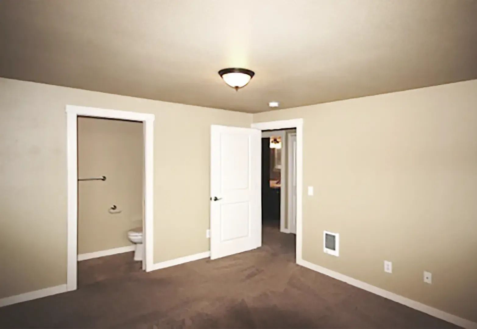 Empty beige bedroom with two open doors, carpeted floor, and ceiling light.