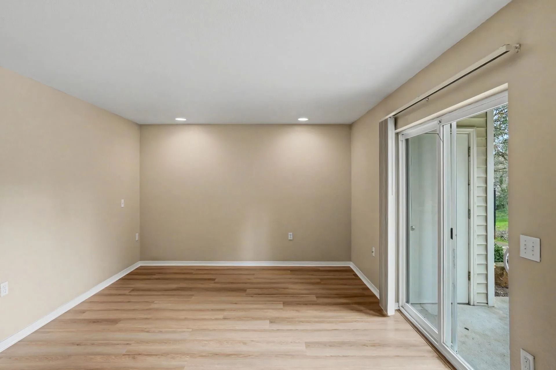 Empty beige living room with wood floor and sliding glass door to patio