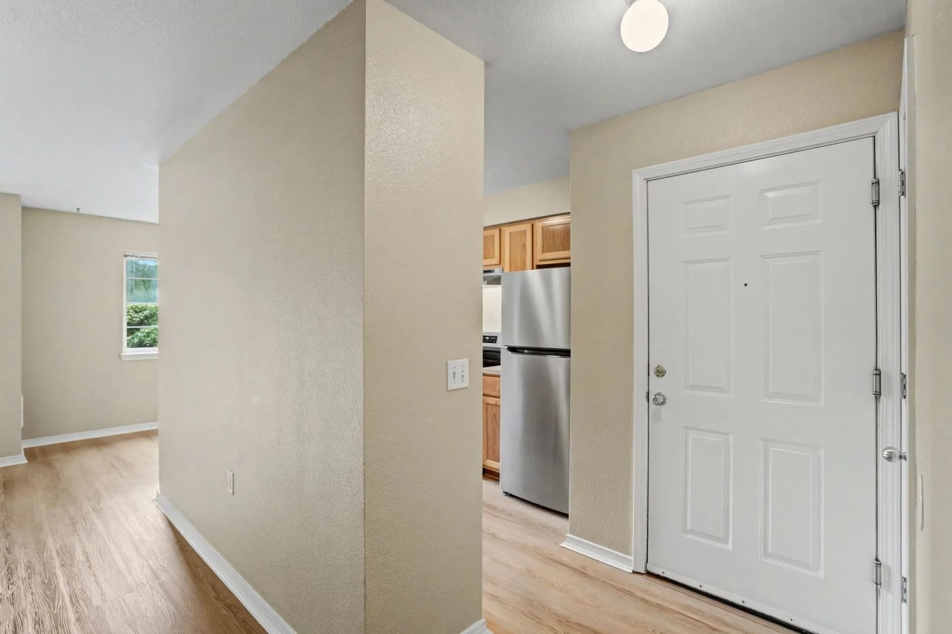 Bright apartment entryway with white front door, beige walls, and light wood flooring.