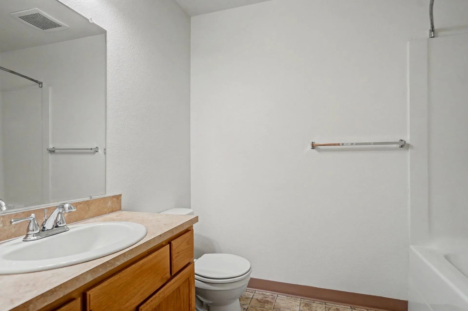 Empty bathroom with white walls, sink vanity, toilet, towel bar, and bathtub visible.