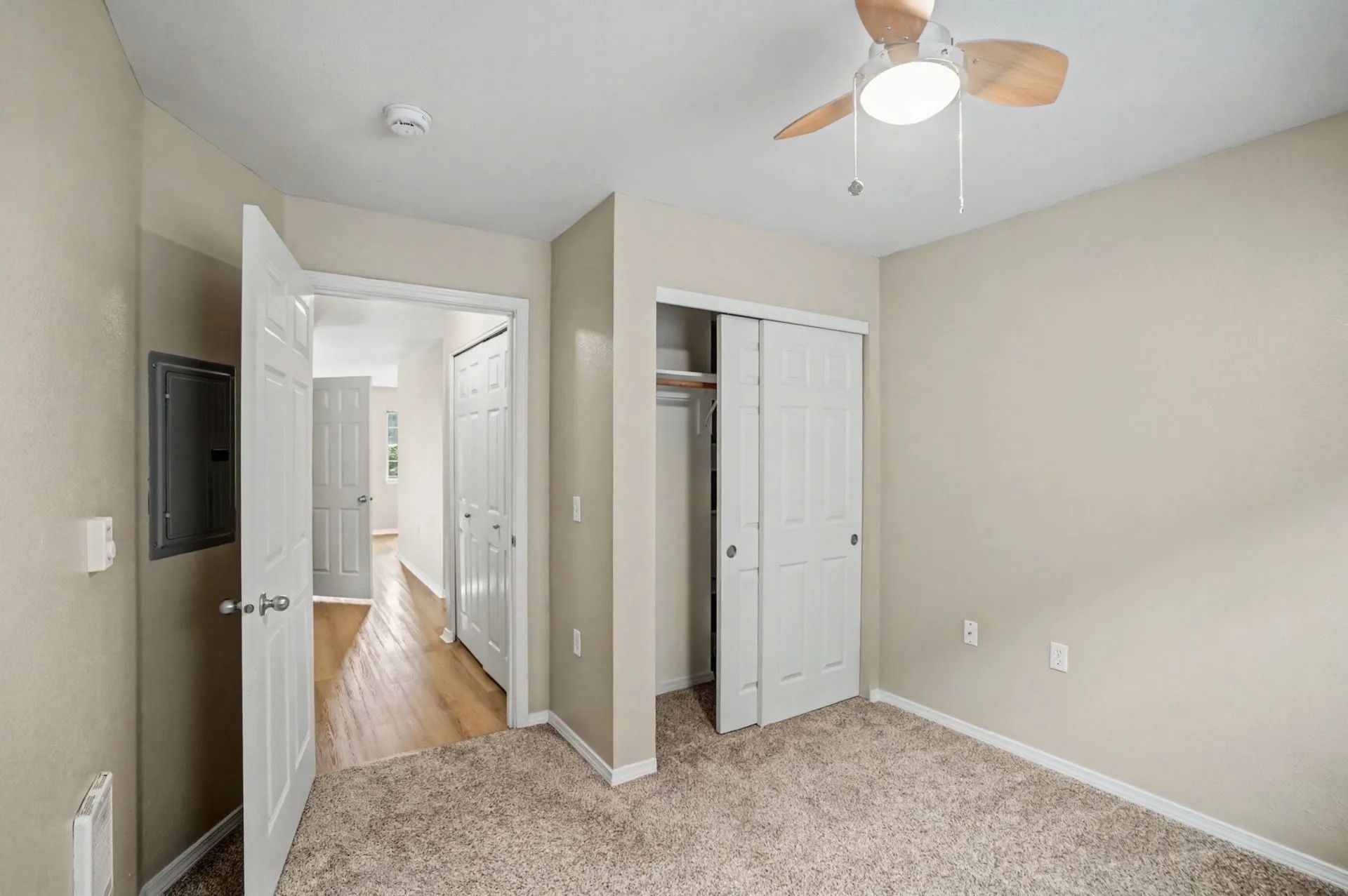 Empty beige bedroom with carpet, ceiling fan, closet, and open door to hallway