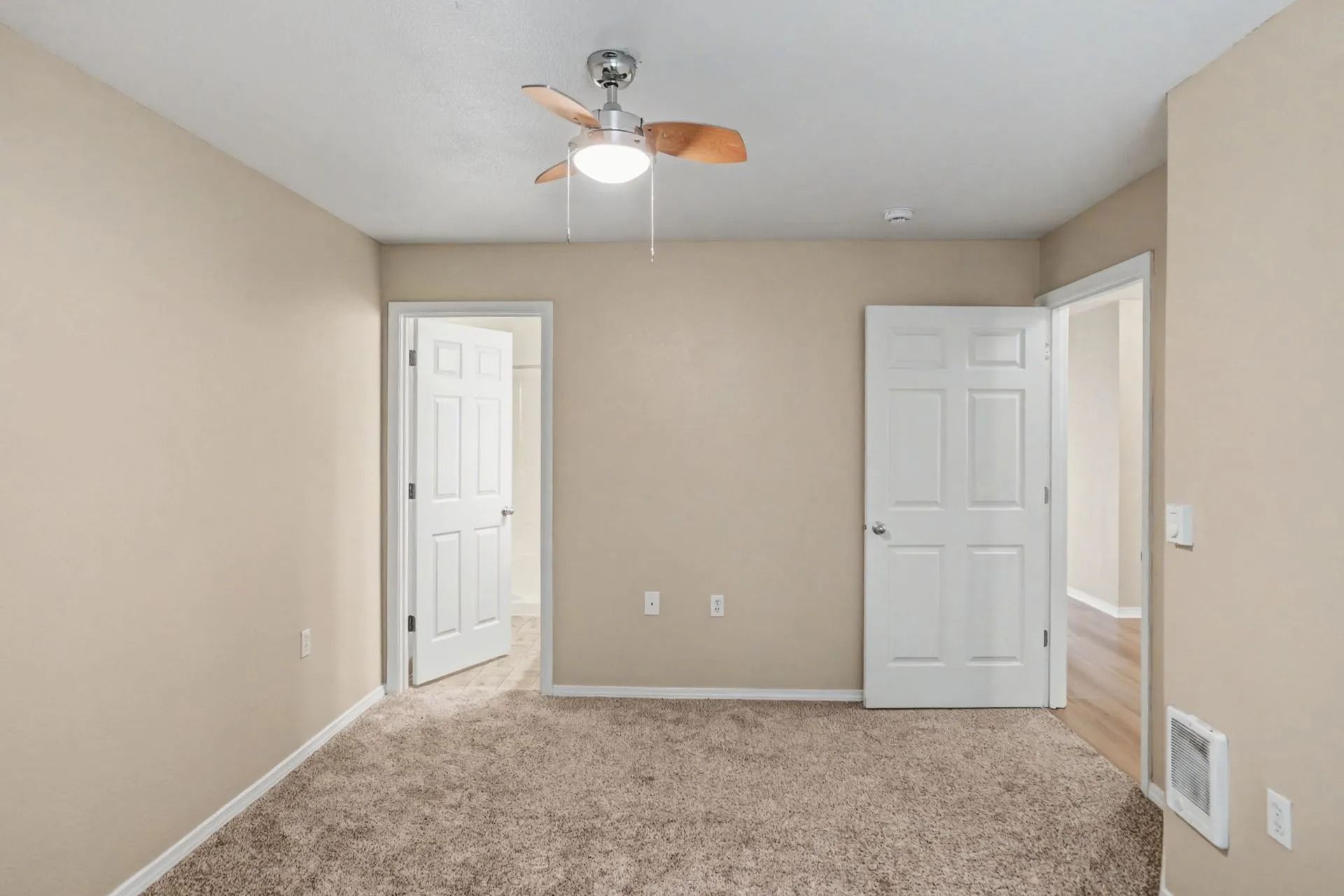 Empty beige bedroom with carpet, ceiling fan, and two white doors.