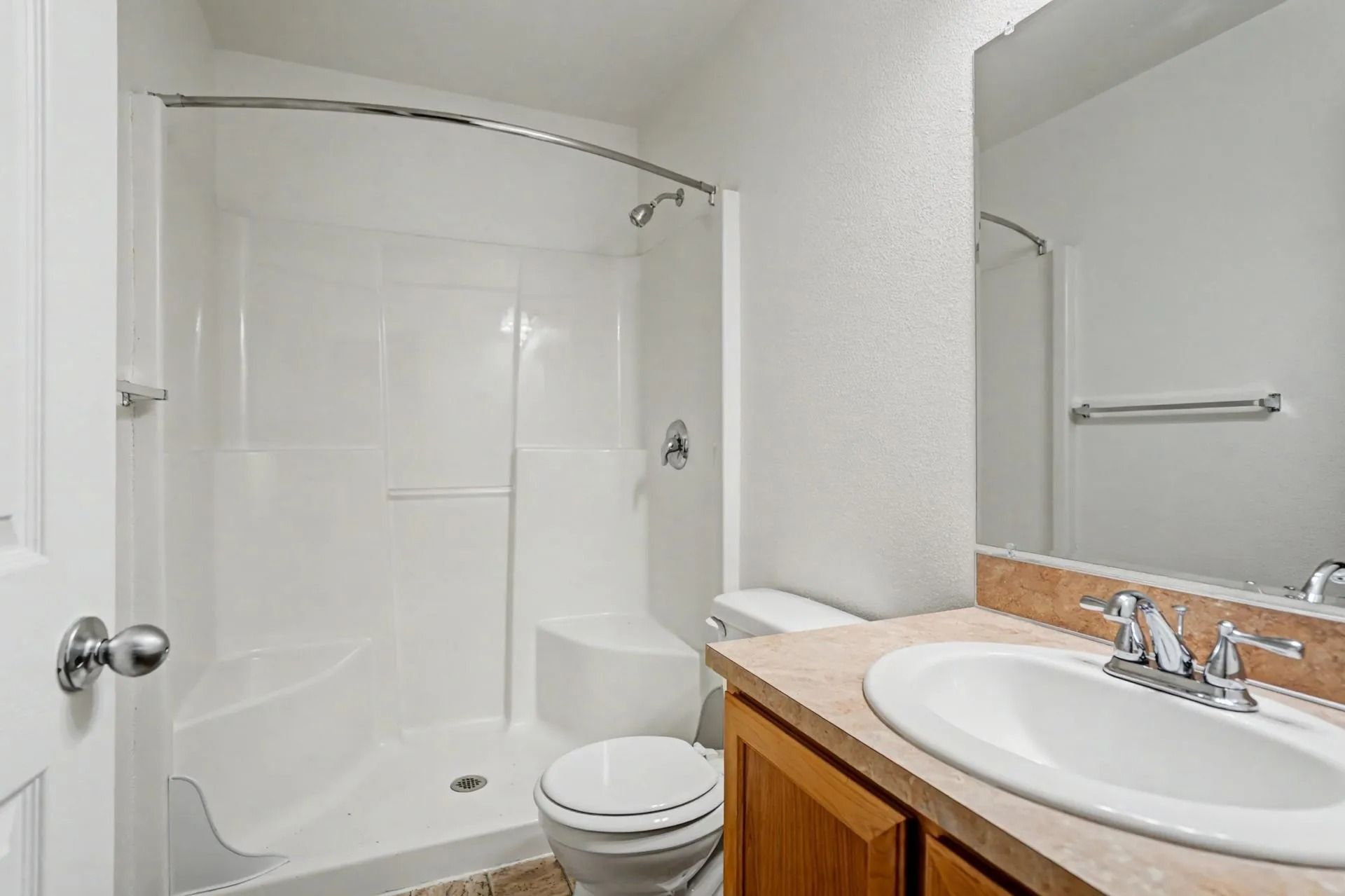 Bright bathroom with shower-tub, toilet, and wooden vanity with white sink and mirror.