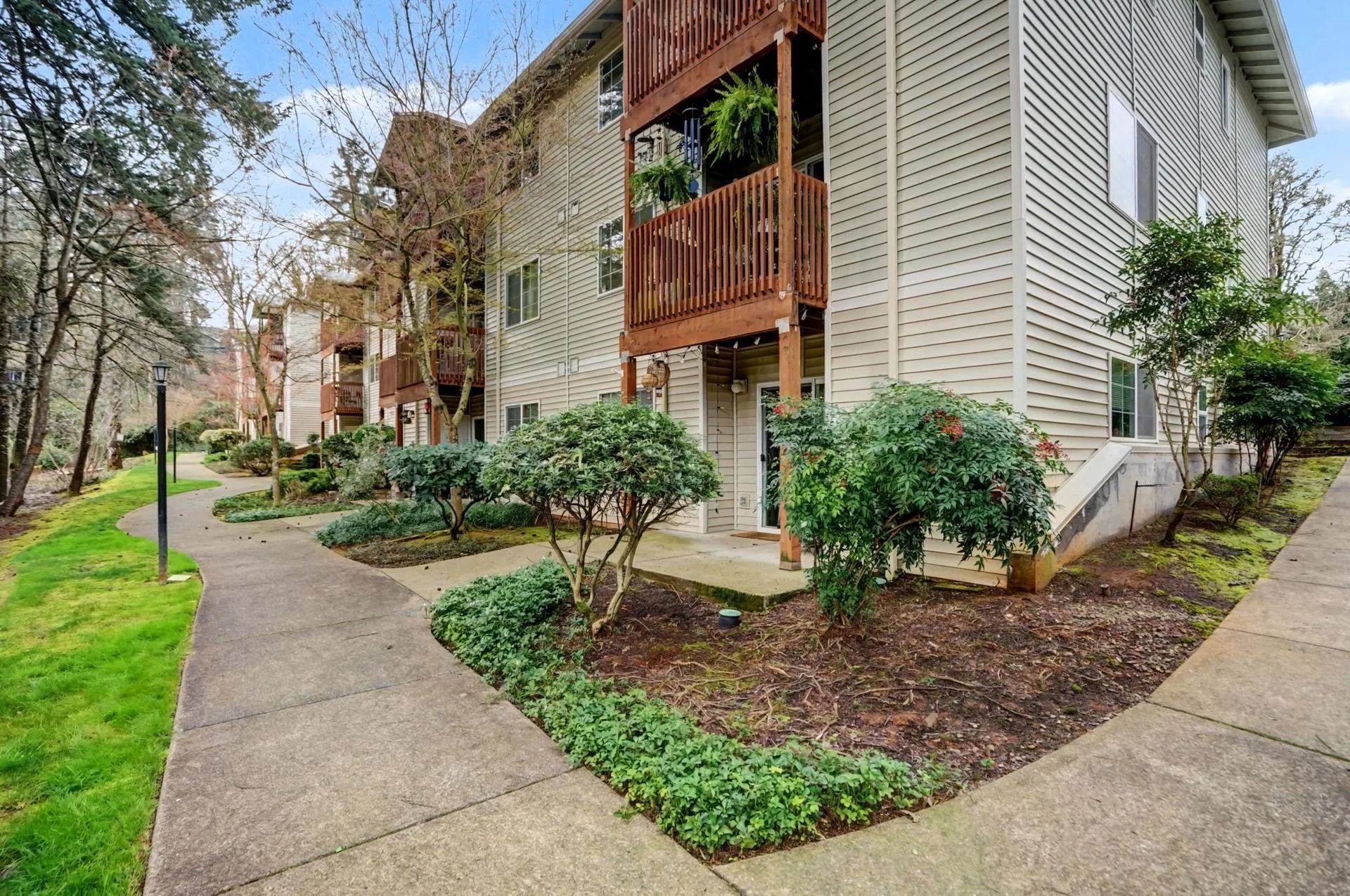 Apartment building with brick balconies beside a winding sidewalk and landscaped greenery