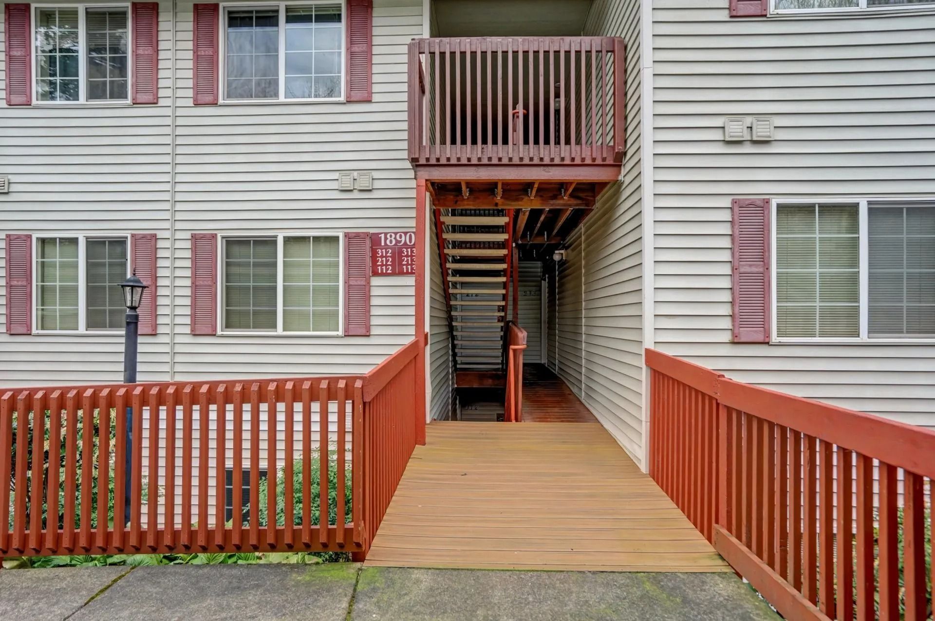 Exterior walkway with red railings leading to apartment stairs and a second-floor balcony