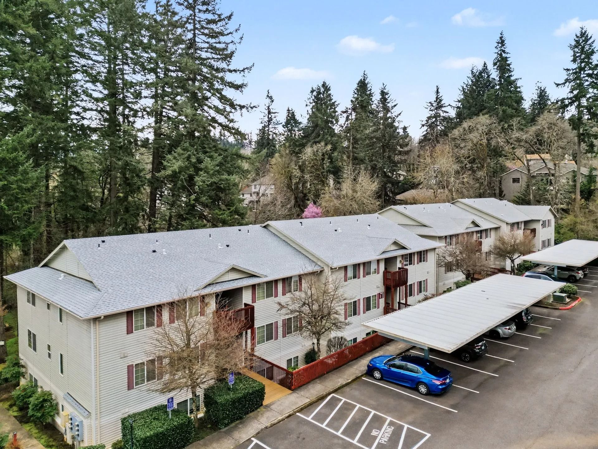 Apartment complex with covered parking, surrounded by tall trees on a hillside.