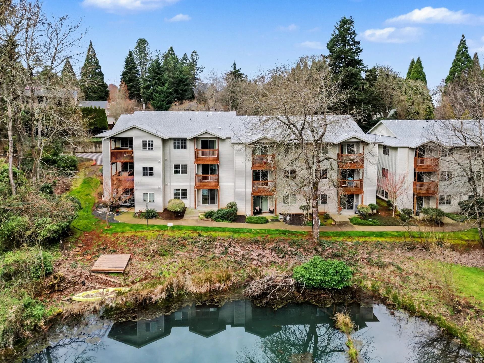 Apartment buildings beside a small pond, surrounded by trees and greenery