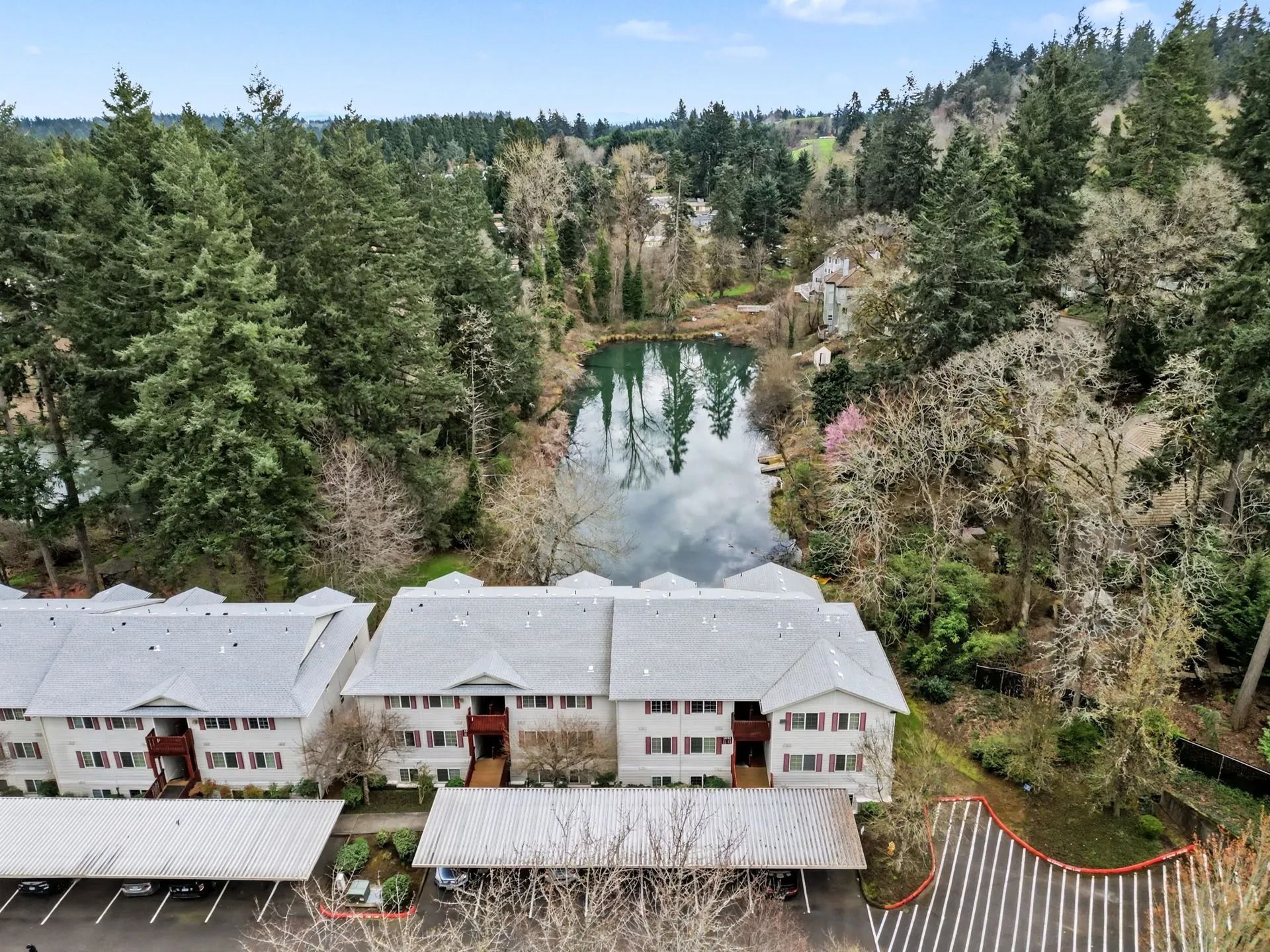 Lakeside lodge with gray roofs amid dense evergreen forest and a small pond in the background