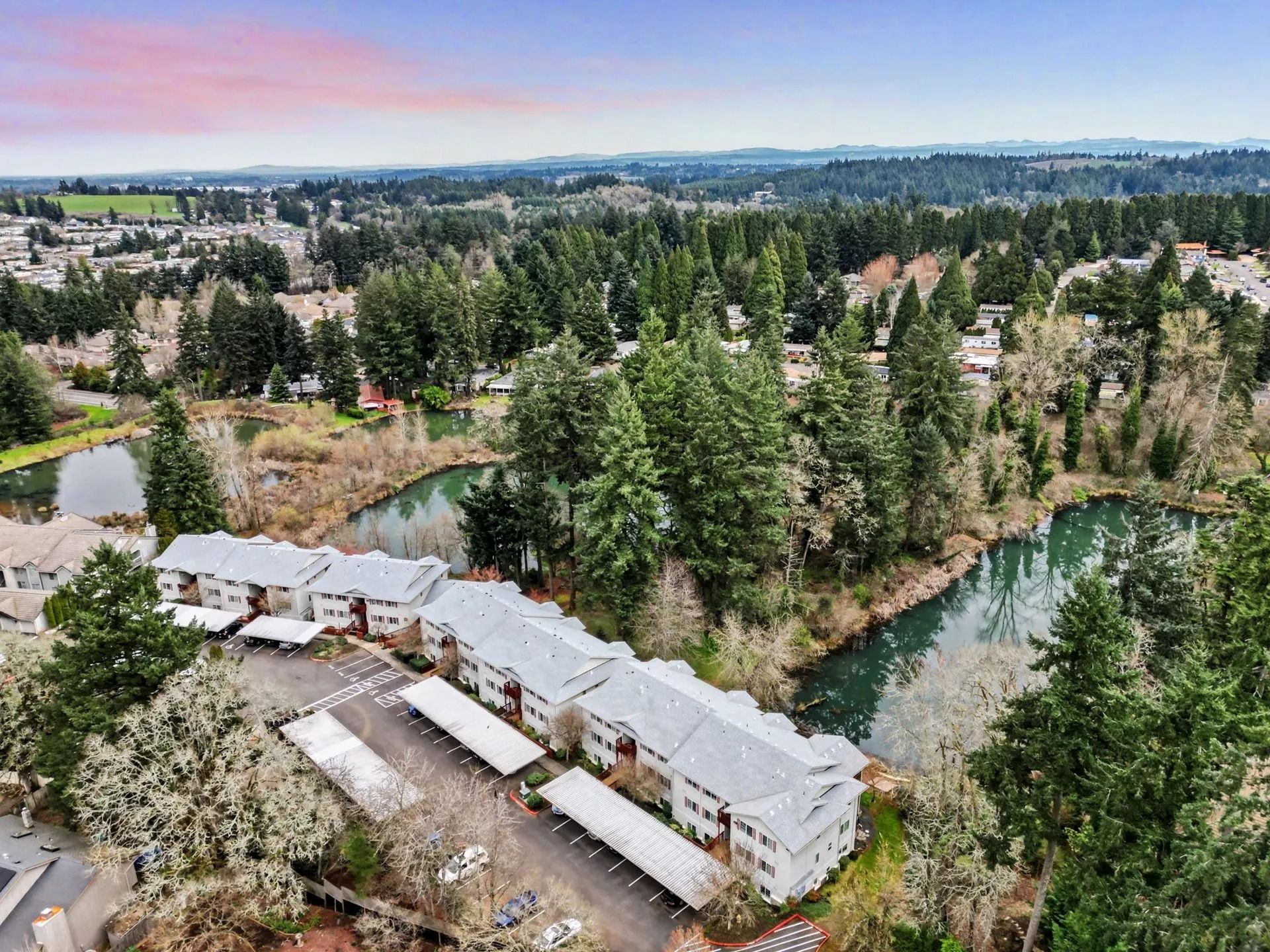 Aerial view of a riverside lodge complex surrounded by trees and water at sunset.