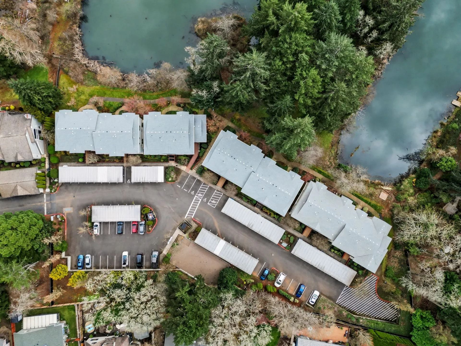 Aerial view of a riverside parking lot, white-roofed buildings, and trees beside water