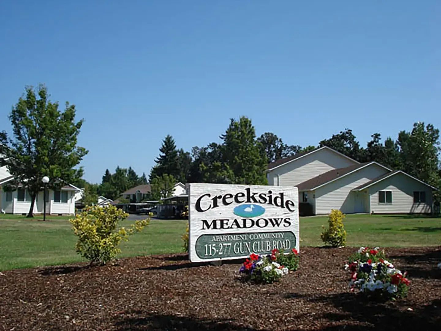 Creekside Meadows entrance sign with flowers in a landscaped neighborhood under a clear blue sky
