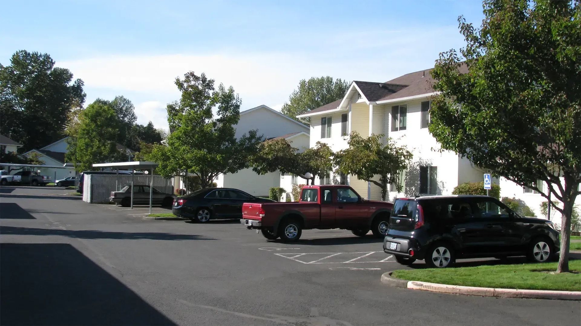 Apartment parking lot with several parked cars and trees on a sunny day