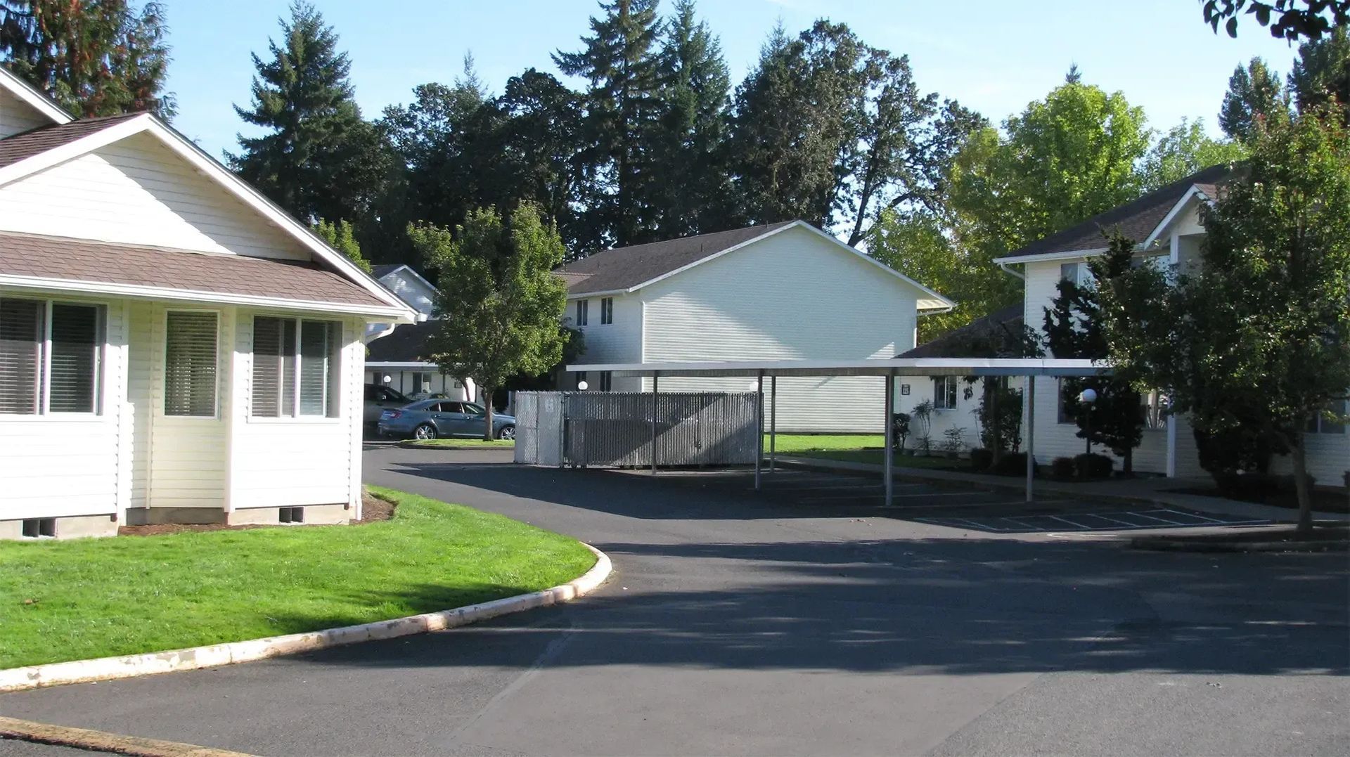 Residential driveway and apartment buildings with a paved lot, trees, and bright sunlight