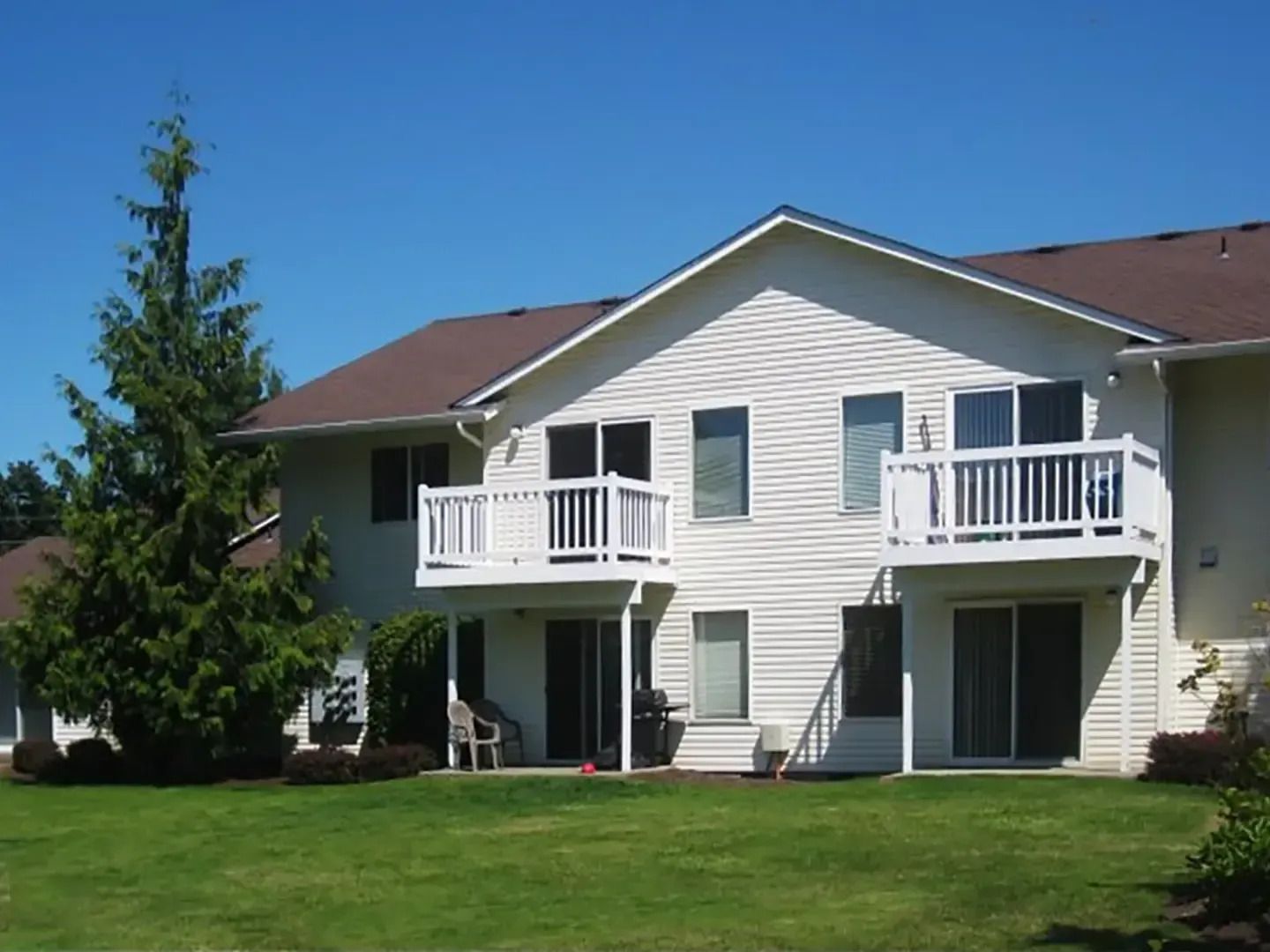 Two-story white apartment building with balconies and green lawn under a blue sky